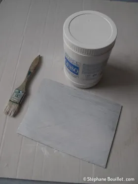 La plaque de linoleum reçoit une fine couche de gesso. Cela a plusieurs objectifs: - permettre de faire un crayonné plus facilement que sur le ton brun foncé - pouvoir décalquer un dessin original (pour le retourner) - blanchir la plaque pour simuler le papier = les parties qui vont rester blanches = les parties à creuser  Une couche suffit mais on peut aussi en mettre plusieurs, poncer entre etc